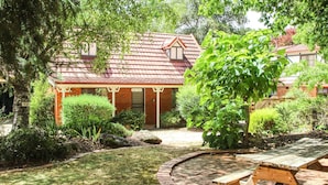 A brick cottage with a red tiled roof, surrounded by lush greenery and a small pond. - AMBER COTTAGE: Bright (Bright)