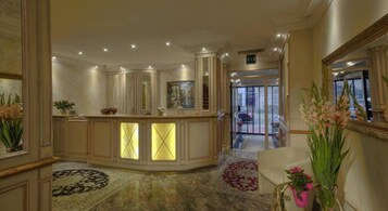 Un vestíbulo de hotel con un mostrador de recepción, un espejo grande y suelo cubierto de alfombra.