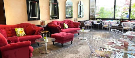 Un área de descanso moderna con sofás rojos, mesas de vidrio transparente y sillas de metal.