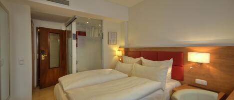 A hotel room with a large bed, a bedside table, a chair, and a wall-mounted lamp.