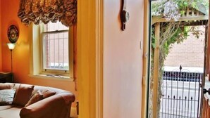 Una habitación con puerta de madera que da a un balcón, ventana con cortina y un reloj en la pared.