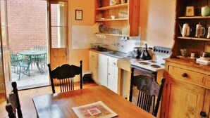 Una cocina con una mesa de comedor, sillas, estufa y estantes con utensilios de cocina.