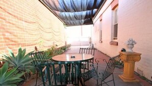 Un patio con una mesa redonda y sillas, rodeado de plantas y un muro de ladrillo.