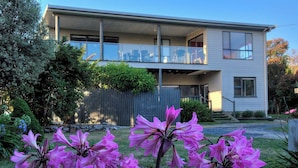 Een tweelaags huis met een balkon, omringd door een tuin met roze bloemen.