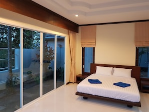 Ein Schlafzimmer mit einem großen Bett, einer Glastür zum Balkon und Blick ins Freie.