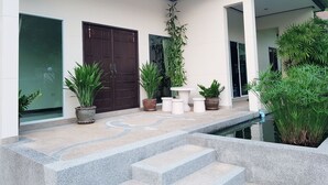 Um edifício moderno com uma entrada ampla, plantas em vasos e uma pequena área de piscina.
