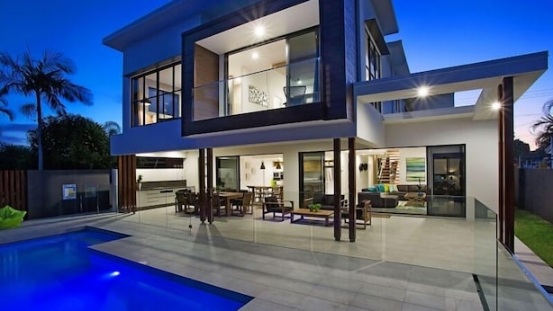 A modern two-story house with a swimming pool, outdoor seating area, and a well-lit interior. - C`est La Vie – Elite Holiday Homes (Gold Coast)