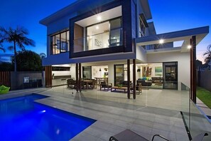 A modern two-story house with a swimming pool, outdoor seating area, and a well-lit interior. - C`est La Vie – Elite Holiday Homes (Gold Coast)
