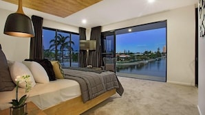 A modern bedroom with a large bed, a TV, and a view of a body of water. - C`est La Vie – Elite Holiday Homes (Gold Coast)