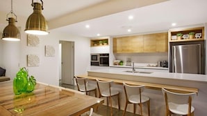 A modern kitchen with a wooden island, stainless steel appliances, and pendant lighting. - C`est La Vie – Elite Holiday Homes (Gold Coast)