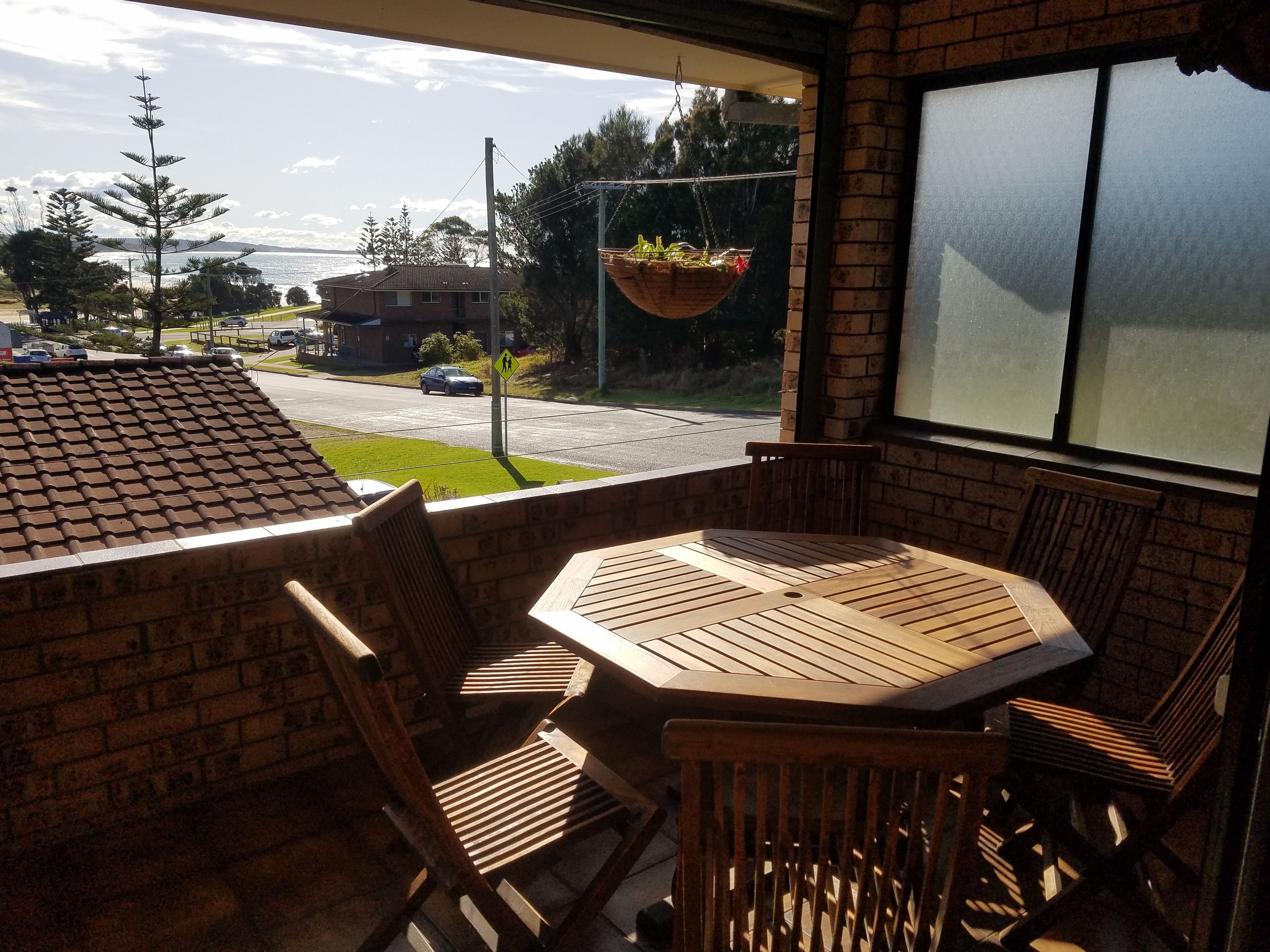 A patio with a brick wall, a hanging planter with plants, and a view of a road and buildings.