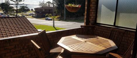 A patio with a brick wall, a hanging planter with plants, and a view of a road and buildings.