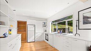 Una cucina moderna con mobili bianchi, pavimento in legno e vista sul verde.