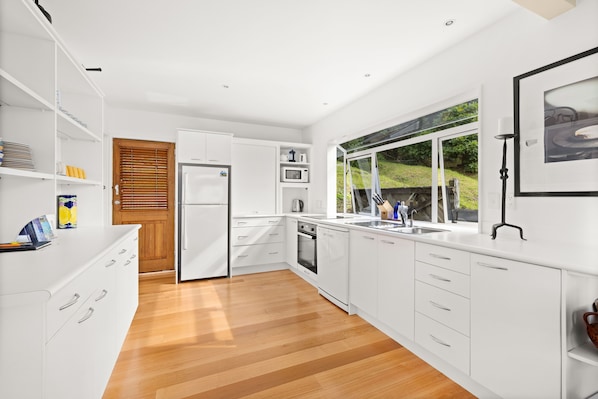 A modern kitchen with white cabinetry, a wooden floor, and a view of greenery outside. - Bayswater Holiday Home, Waterfront Paihia, Bay of Islands (Paihia)
