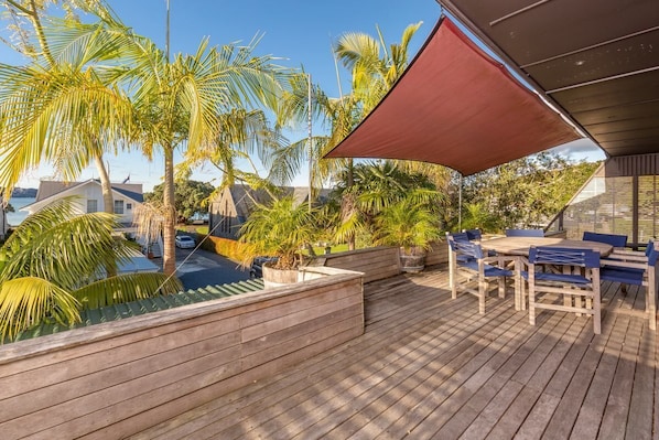 A wooden deck with a table and chairs, surrounded by palm trees and a swimming pool.