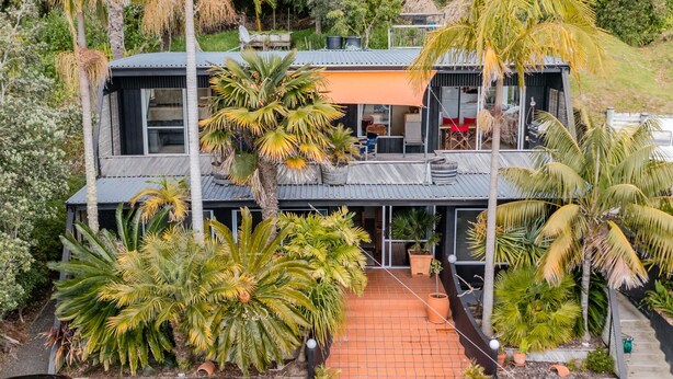 Una moderna casa a due piani con tetto piatto, circondata da rigogliosa vegetazione tropicale.