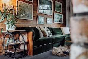 Un sofá verde con varios cojines, una mesa de madera con una planta y cuadros en la pared.