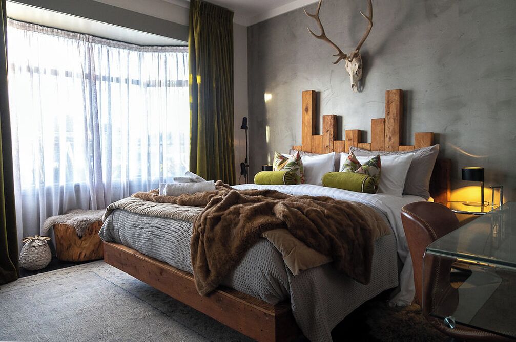 A bedroom with a wooden bed, a mounted deer skull, and a glass coffee table.