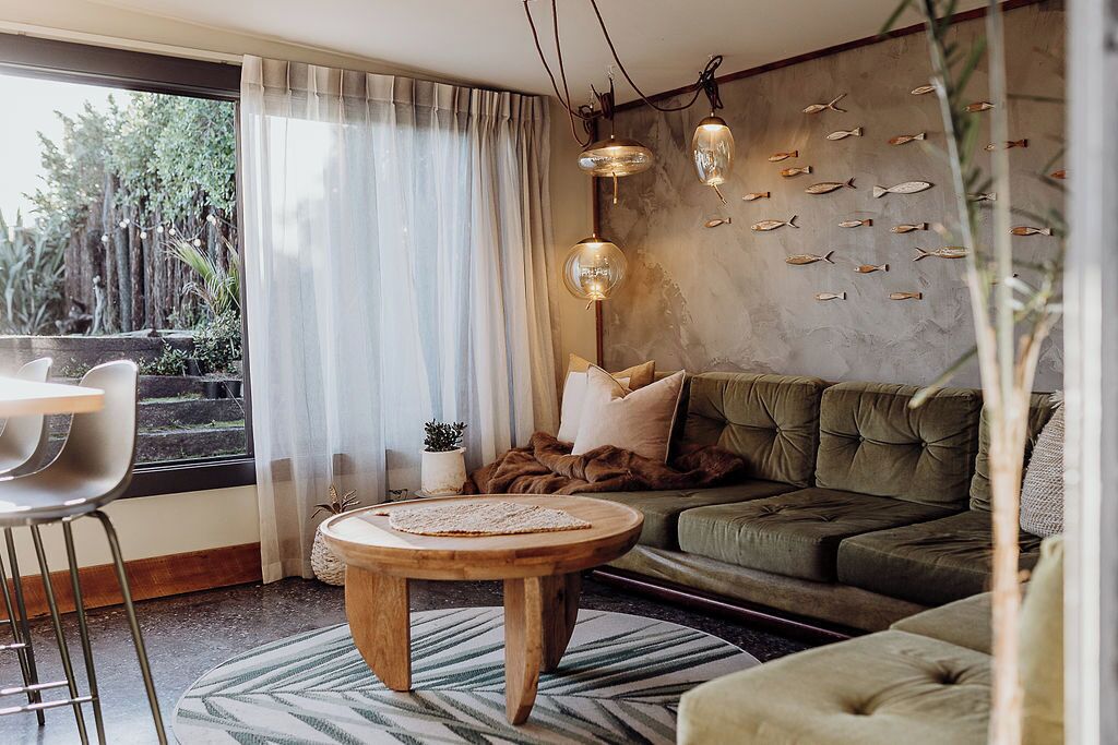 A modern living room with a green sofa, a round wooden coffee table, and a dining area with a white chair.