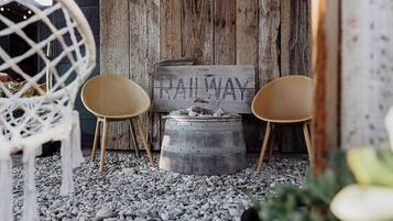A rustic outdoor seating area with two woven chairs, a wooden barrel, and a sign that reads 'RAILWAY.'