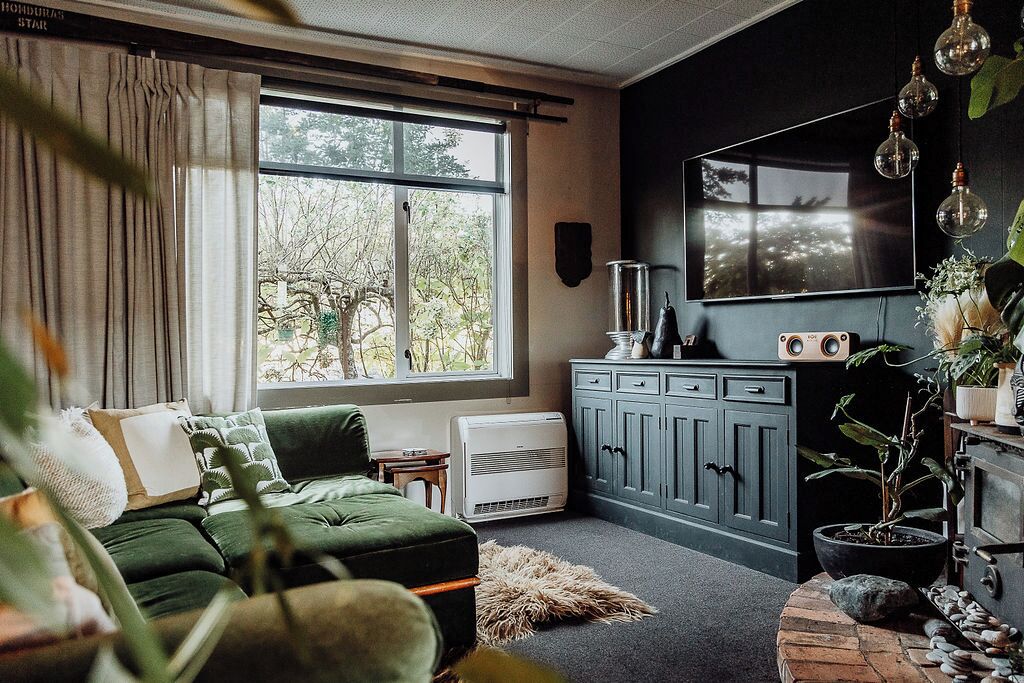 A living room with a green sofa, a fireplace, a TV, and a window with a view of trees.