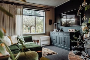 Una sala de estar con un sofá verde, una chimenea, un televisor y una ventana con vistas a árboles.