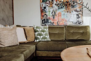 A living room with a green sofa, patterned cushions, and a wall art piece.
