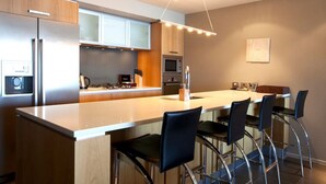 Une cuisine moderne dotée d’un îlot central, de tabourets de bar, d’appareils électroménagers en acier inoxydable et d’un luminaire suspendu.