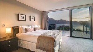 Une chambre d’hôtel avec un grand lit, une table de chevet, une lampe et une vue sur la mer par une grande fenêtre.