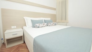 A neatly made bed with a light blue blanket, a wooden headboard, and two floral pillows. - Comfort One-Bedroom Apartment With Balcony and Swimming Pool (Trogir)