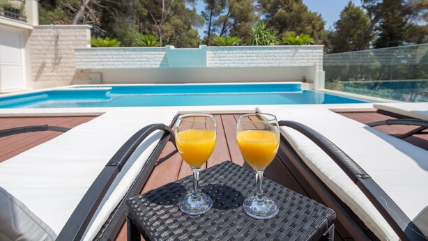 A poolside area with lounge chairs and two glasses of orange juice on a table. - Comfort One-Bedroom Apartment With Balcony and Swimming Pool (Trogir)