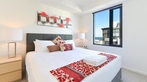Una camera d'albergo moderna con un letto grande, un comodino, una lampada da tavolo, una finestra con vista e un'opera d'arte appesa al muro.
