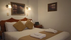 Una cama bien hecha con sábanas blancas y dos almohadas marrones, un cabecero de madera y una manta marrón.