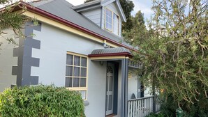 Una casa de dos pisos con fachada gris, techo rojo y un pequeño porche con barandilla blanca.