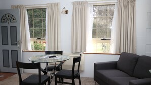 Una habitación con una mesa de vidrio, dos sillas, un sofá y dos ventanas con cortinas.