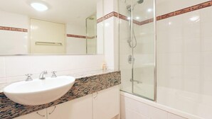 Un baño con lavamanos blanco, cabina de ducha con mampara de vidrio y espejo con detalle de mosaico decorativo.