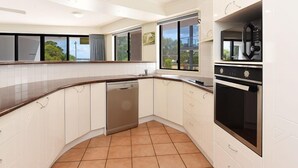 Cocina moderna con armarios blancos, lavavajillas, estufa y un ventanal con vistas a zonas verdes.