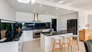 Une cuisine moderne dotée d’un îlot central, d’appareils électroménagers en acier inoxydable et d’une grande fenêtre offrant une vue sur l’extérieur.