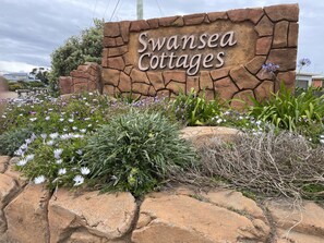 Une enseigne indiquant l’emplacement de « Swansea Cottages », avec un mur en pierre et un jardin agrémenté de diverses fleurs.