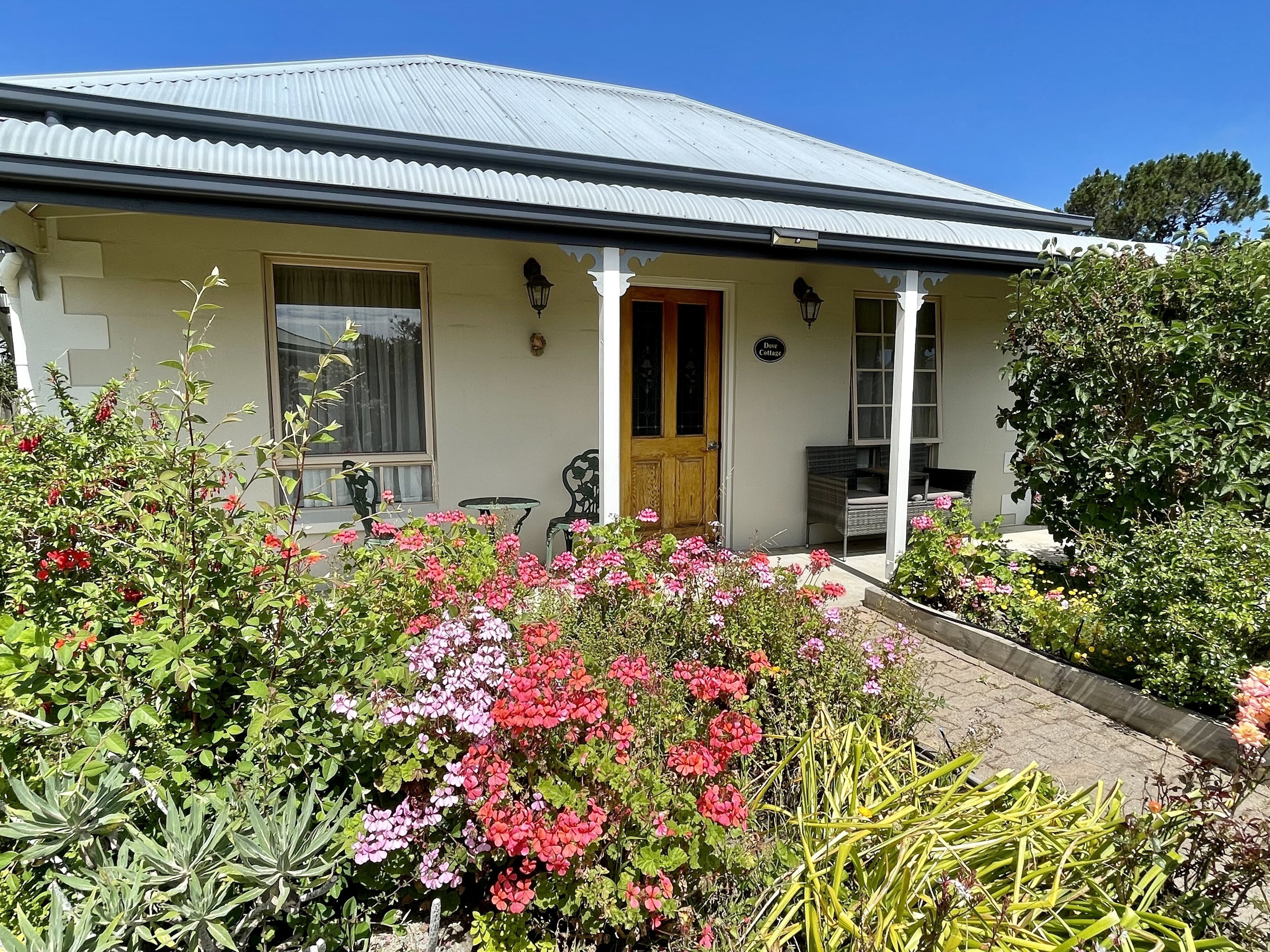 A two-story house with a corrugated metal roof, a front porch with a wooden door, and a garden with various plants and flowers.