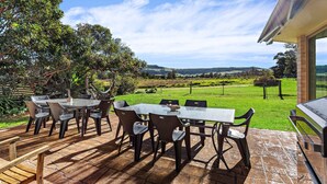 Patio esterno con tavolo e sedie, un'amaca e vista su un prato e delle colline sullo sfondo.