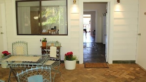 A room with a metal table, chairs, a potted plant, and a window with a view of greenery. - Bickley Valley Cottage (Bickley)