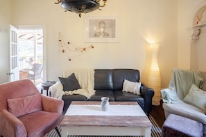 Ein Wohnzimmer mit einer schwarzen Ledersofa, einem pinken Sessel, einem Holztisch und einer Lampe.