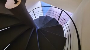 Una escalera de caracol con barandilla negra y pared blanca con dos cuadros enmarcados.