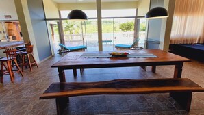 Un comedor amplio con una gran mesa de madera, bancos y vistas a una piscina y vegetación exterior.