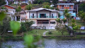 Una casa de dos pisos con balcón, rodeada de follaje y una masa de agua.
