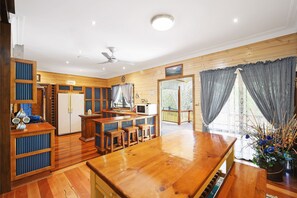 A spacious kitchen with wooden cabinets, a dining area with a large wooden table, and a view of the outdoors through large windows.