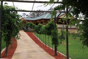 A pathway leading to a building with a green roof, surrounded by trees and a well-maintained lawn.