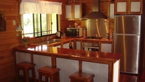 Una cocina con armarios de madera, un refrigerador de acero inoxidable, una estufa y un lavamanos. Hay tres taburetes de madera alrededor de la barra.