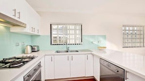 Una cocina moderna con armarios blancos, cocina a gas, un lavamanos y una ventana con persianas.